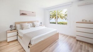 A bedroom with a bed, bedside tables, a window with a view of palm trees, and a built-in wardrobe. - Th88 Apartamento en Miami Playa (Mont-roig del Camp)