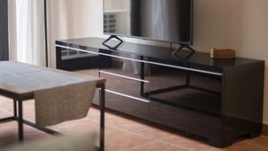 A modern room with a flat-screen TV on a dark wooden cabinet, a glass table, and a chair. - Th86 Apartamento con Encanto en Parte Alta (Tarragona)