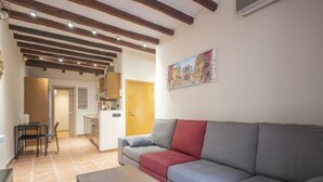 A living room with a grey sofa, a red pillow, and a wooden coffee table. There is a painting on the wall and a kitchen area in the background. - Th86 Apartamento con Encanto en Parte Alta (Tarragona)