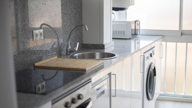 A modern kitchen with a granite countertop, stainless steel sink, and built-in appliances including a dishwasher and oven. - Th64 Apartamento Moderno Cerca de la Universidad (Tarragona)