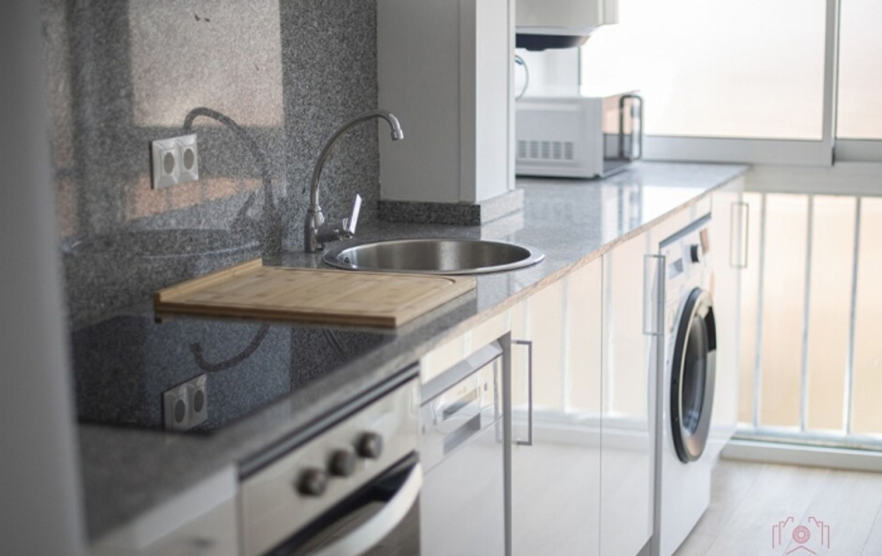 A modern kitchen with a granite countertop, stainless steel sink, and built-in appliances including a dishwasher and oven.