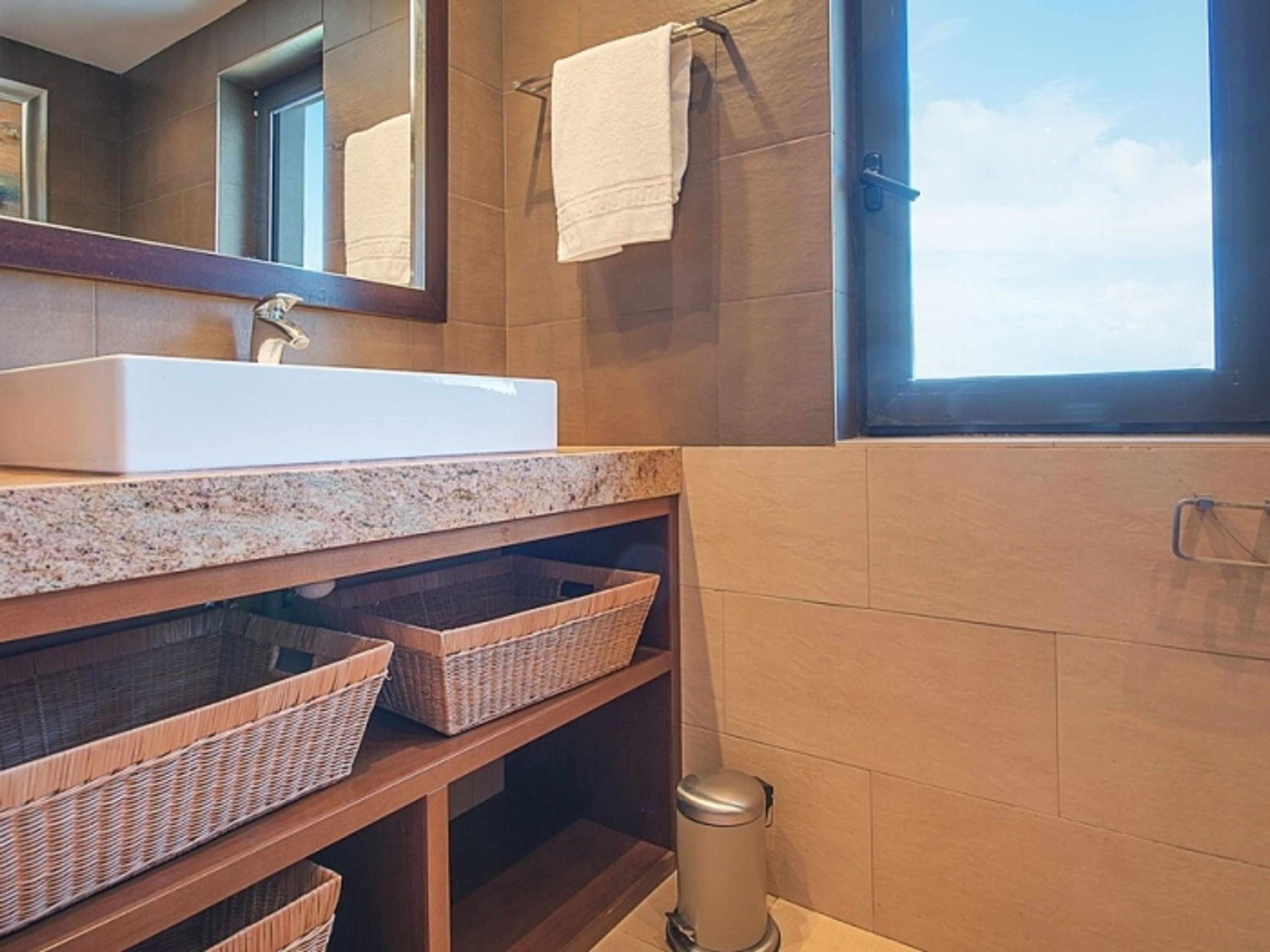 A bathroom with a white sink, wicker baskets, a mirror, and a window.