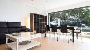 A modern living room with a sofa, a glass coffee table, a bookshelf, and a dining area with chairs and a table. - Th52 Torredembarra Elegante Villa Vistas al mar (Torredembarra)