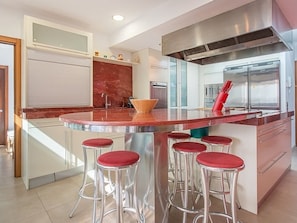Uma cozinha moderna com ilha central, eletrodomésticos de aço inoxidável e banquetas.