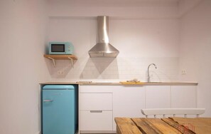 A compact kitchen with a blue refrigerator, a stainless steel range hood, and a white sink.