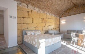 Un dormitorio con pared de piedra, una cama con colcha de lunares, una mesita con sillas y un sofá.