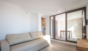 Una sala moderna con un sofá color beige, un aparador de madera y un ventanal corredero que da a un comedor.