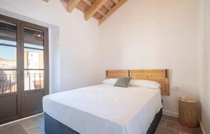 Un dormitorio con una cama grande, un cabecero de madera, una mesita de noche pequeña y una ventana con vistas.