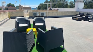 Une terrasse sur le toit, aménagée avec du mobilier d’extérieur, comprenant deux fauteuils en osier et une petite table, ainsi qu’un tabouret jaune.