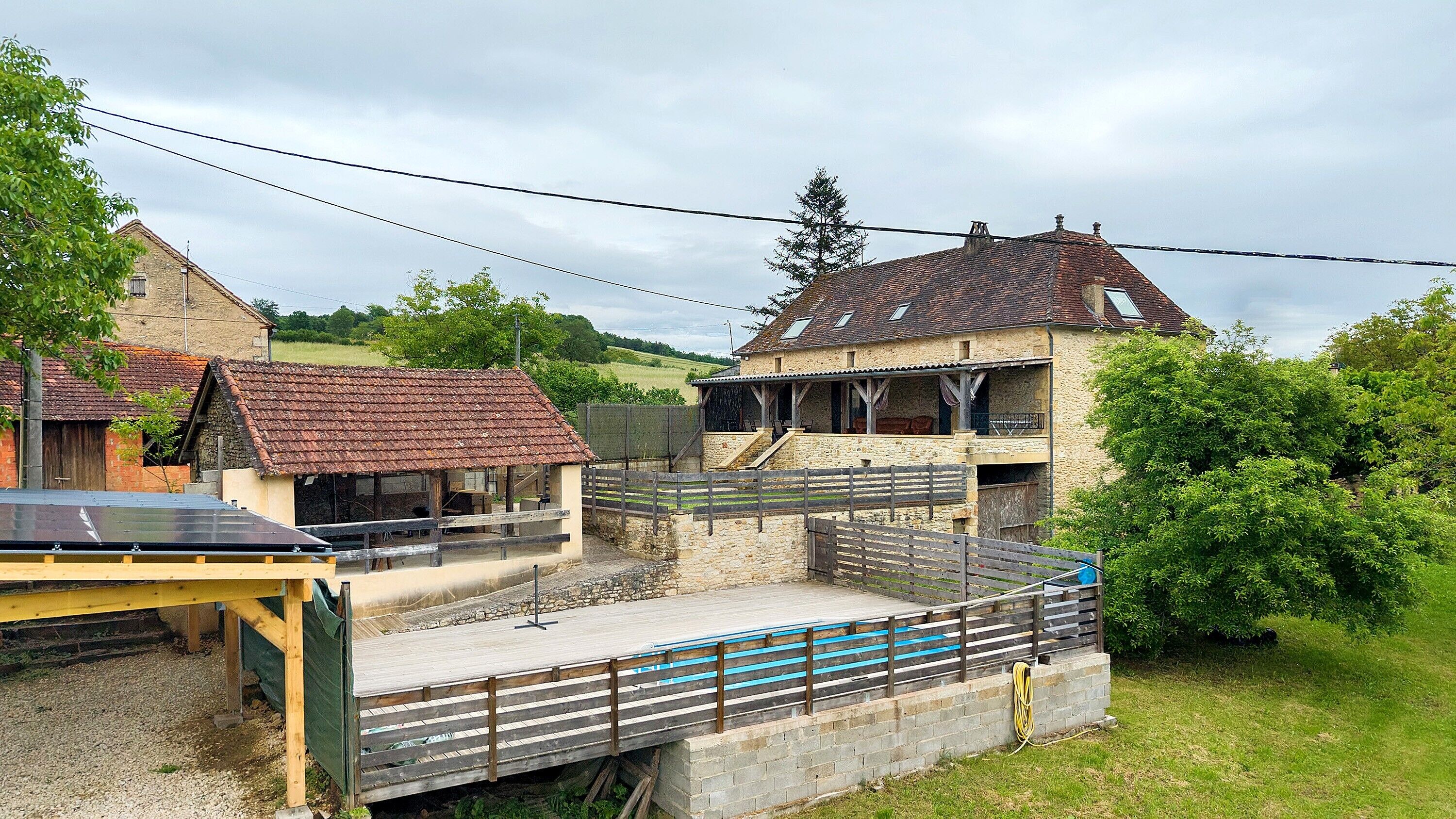 Un edificio rustico con facciata in pietra, un patio in legno e un piccolo spazio esterno con posti a sedere.