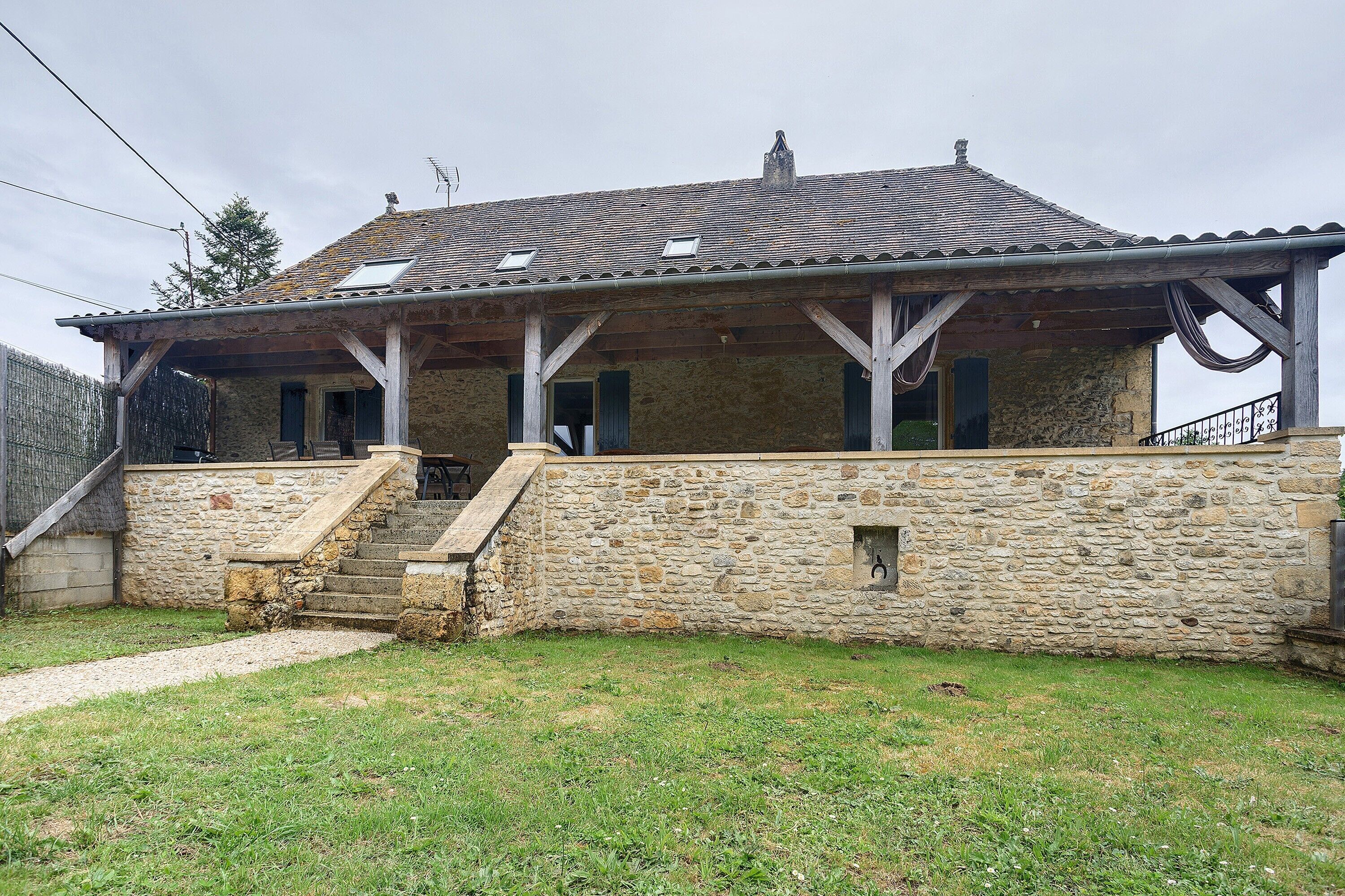 A stone house with a covered porch, a stone staircase, and a grassy yard.