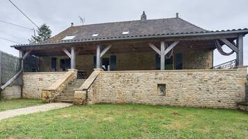 A stone house with a covered porch, a stone staircase, and a grassy yard.