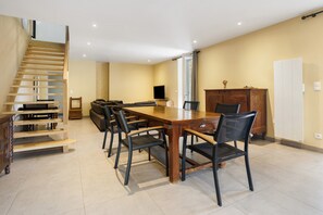 A spacious dining area with a wooden table and chairs, a built-in TV, and a staircase leading to an upper level.