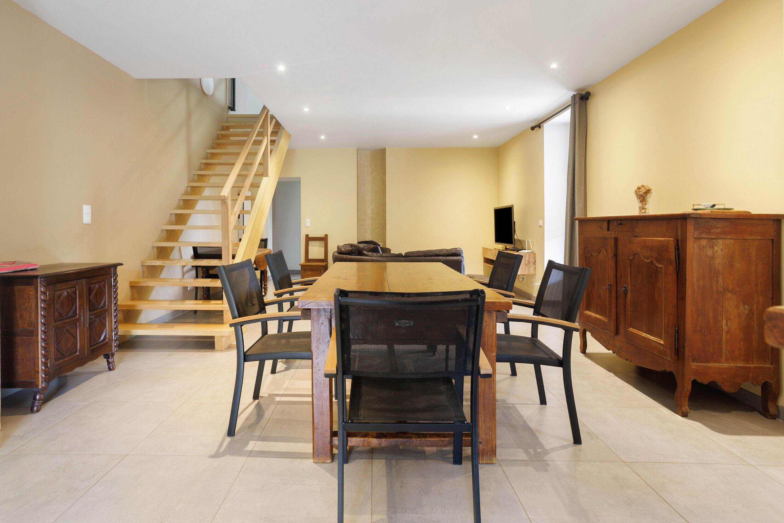 Un comedor con una mesa y sillas de madera, una escalera y un armario de madera.