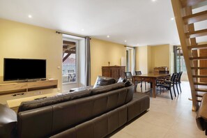 A living room with a sofa, TV, dining table, chairs, and a staircase.