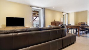 A modern living room with a large leather sofa, a flat-screen TV, a dining table with chairs, and a wooden cabinet. - Charming House in the Heart of the Périgord Noir – Private Pool & Preserved Nature (Siorac-en-Périgord)