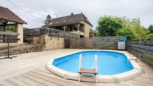 A swimming pool with a wooden deck, a stone wall, and a house with a tiled roof. - Charming House in the Heart of the Périgord Noir – Private Pool & Preserved Nature (Siorac-en-Périgord)