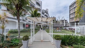 Una entrada con portón a un complejo residencial con un corredor cubierto, palmeras y una cerca blanca.
