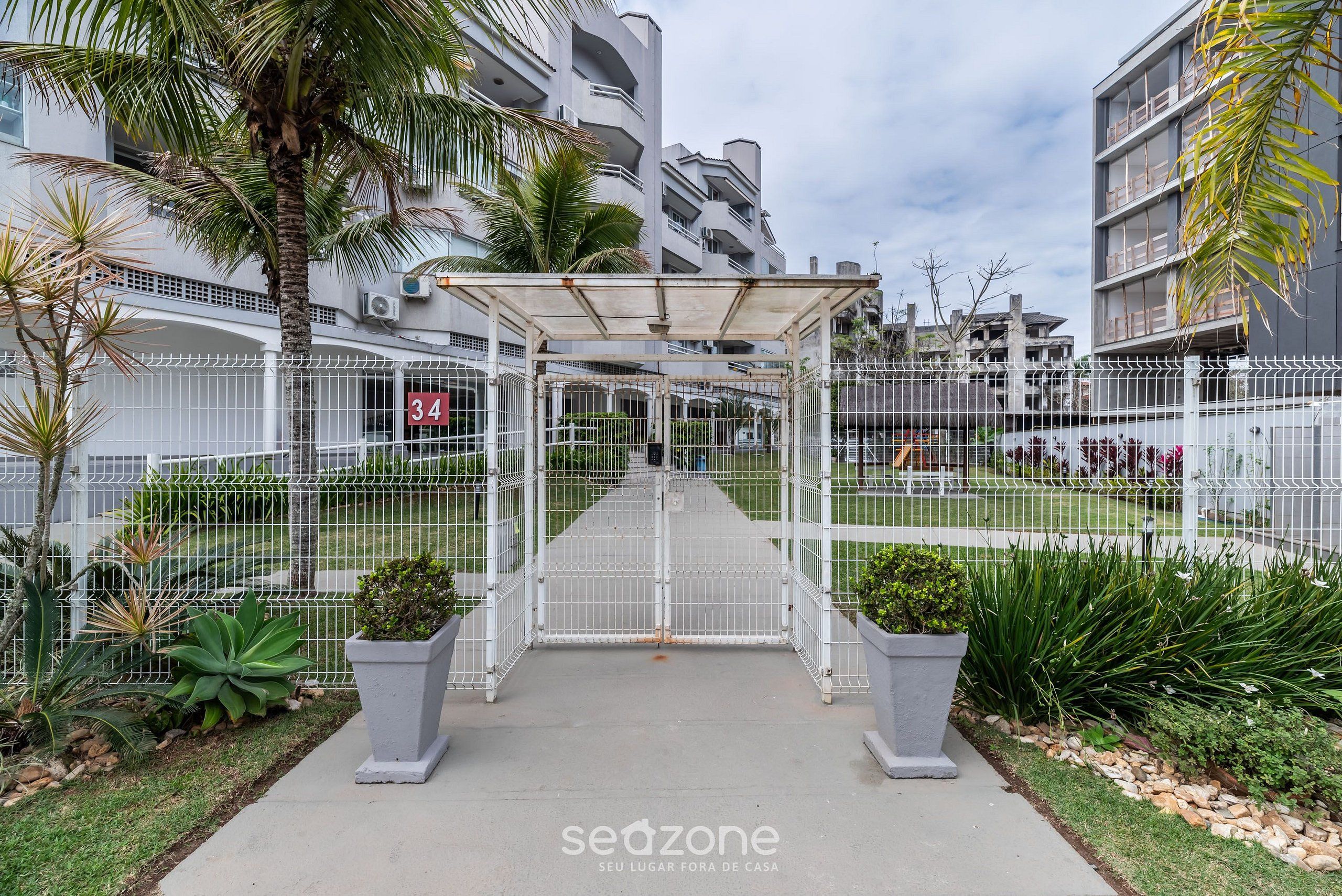 A gated entrance to a residential complex with a covered walkway, palm trees, and a white fence.