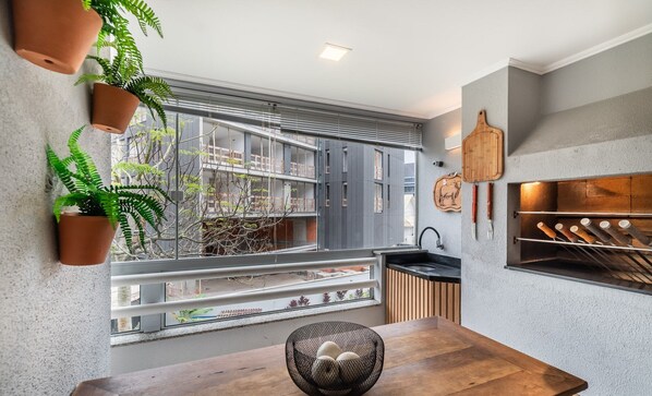 A modern kitchen with a large window, a wooden dining table, and potted plants.