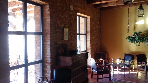 A rustic room with stone walls, wooden furniture, and large windows. - CASA RURAL AMANECER (Castañar de Ibor)