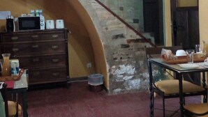 A room with a stone wall, a wooden staircase, a dining table with chairs, and a small kitchen area with a microwave and other appliances. - CASA RURAL AMANECER (Castañar de Ibor)