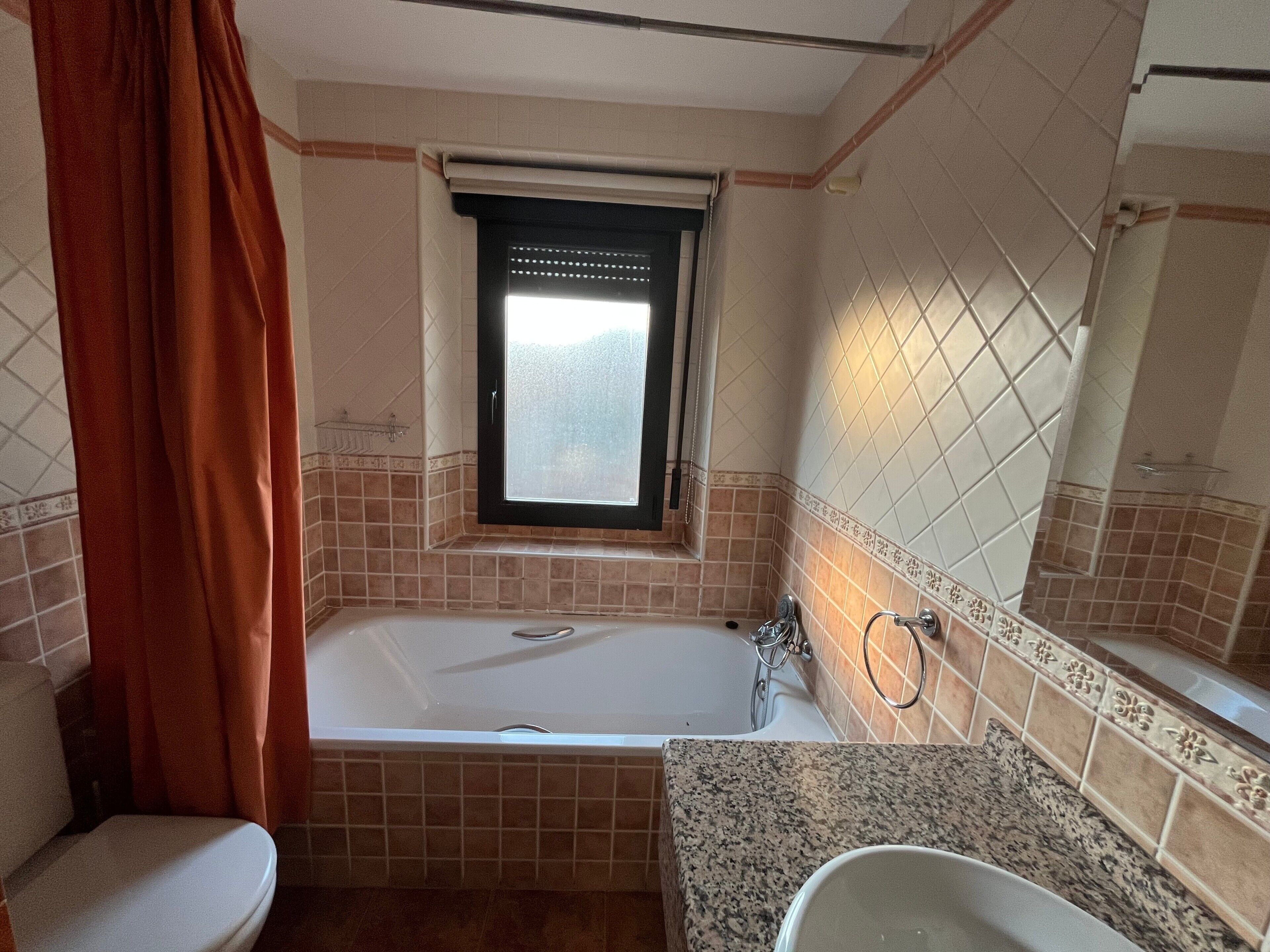 Un baño con bañera, inodoro, lavamanos y ventana.