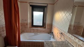 Un baño con bañera, inodoro, lavamanos y ventana.