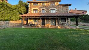 A two-story stone house with a patio area, outdoor seating, and a well-maintained lawn.