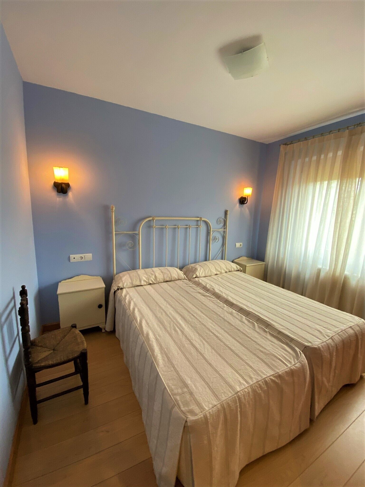 Un dormitorio con una cama doble, mesitas de noche, una silla y una ventana con cortinas.