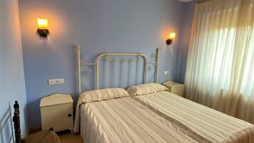 Un dormitorio con una cama doble, mesitas de noche, una silla y una ventana con cortinas.