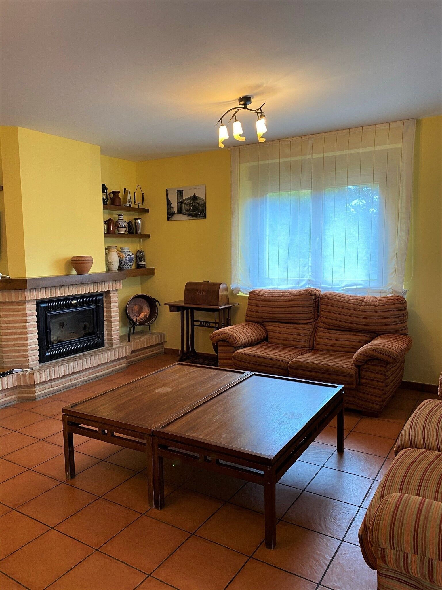 Una sala de estar con chimenea, un sofá, una mesa de centro y un ventanal con cortinas.