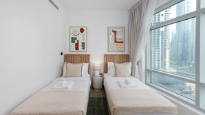 Une chambre d’hôtel avec deux lits, une vue sur de hauts immeubles et des œuvres d’art abstrait accrochées au mur.