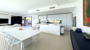 Une cuisine moderne avec des meubles blancs, un îlot central et un coin repas avec des chaises blanches.