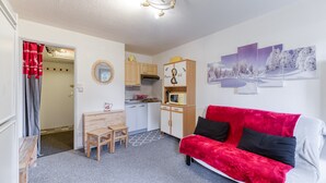 A compact living space with a kitchenette, a red sofa, a dining table, and a small wooden chair.