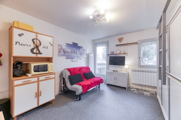 A compact living space with a kitchenette, a red sofa, a television, and a window.