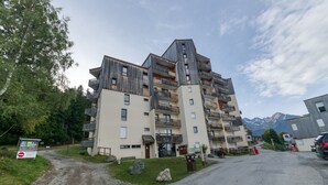 A multi-story building with balconies, a gravel path, and a mountain in the background.