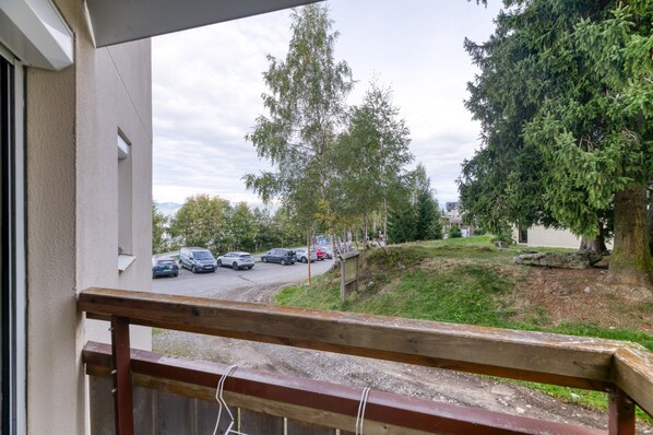 Un balcon d’où l’on peut voir des voitures garées, des arbres et un bâtiment au loin.