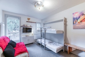 A room with bunk beds, a TV, a desk, a window with a view, and a red couch.