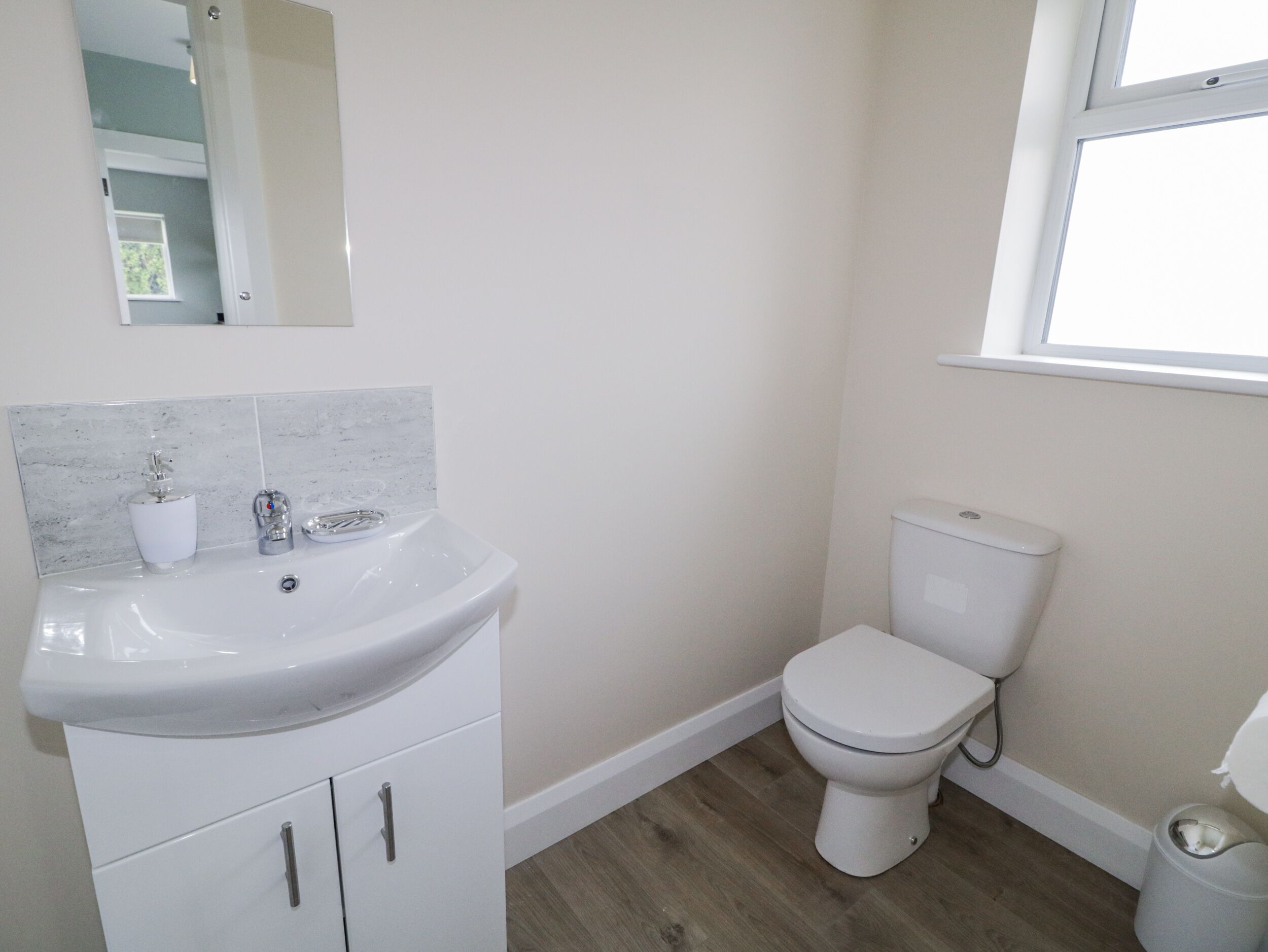 A bathroom with a white sink, toilet, and a window.