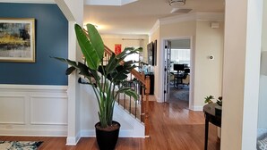 Un interior de vivienda amplio y de varios niveles, con suelos de madera, una escalera central y una gran planta en maceta.