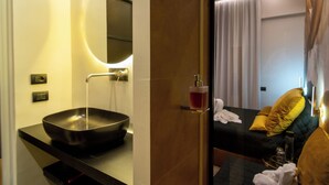 A modern bathroom with a black vessel sink, a round mirror, and a bottle of hand soap on the wall. - Luxury Procida in Naples station train (Napoli)