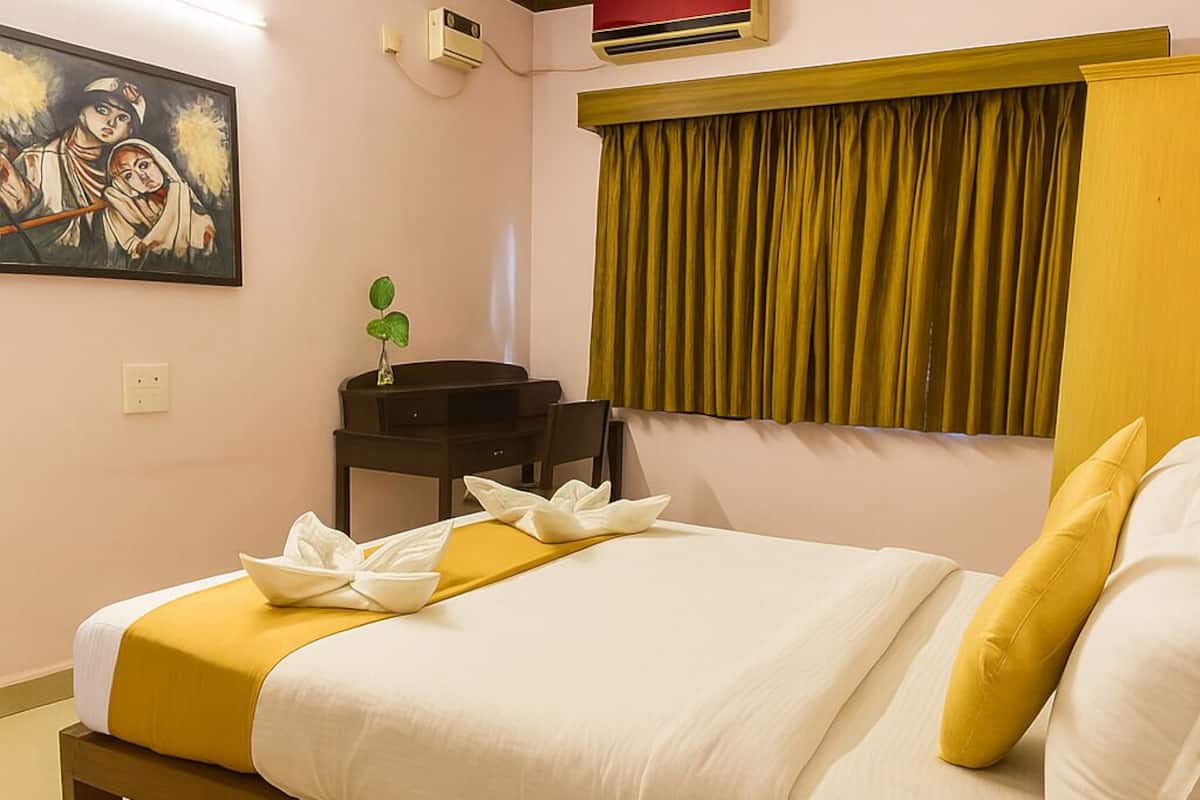 A hotel room with a bed, a desk, a chair, a ceiling fan, a painting, and a window with curtains.