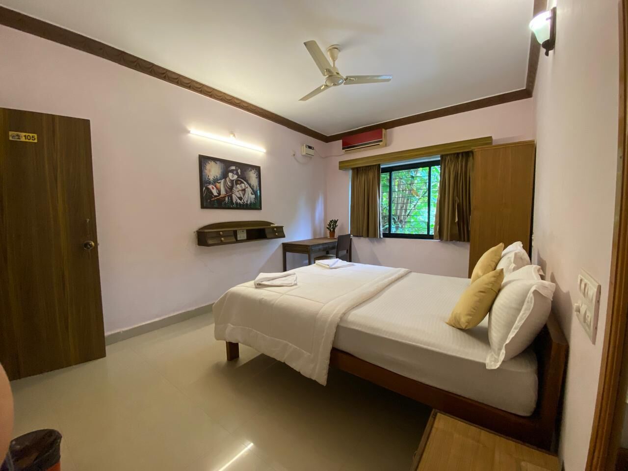 Une chambre d’hôtel équipée d’un lit, d’un bureau, d’une chaise, d’un ventilateur de plafond et d’une fenêtre avec des rideaux.