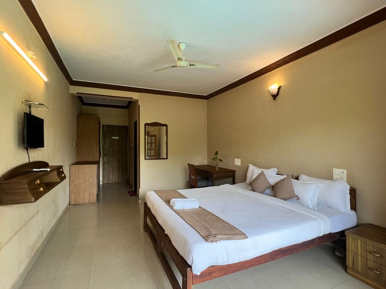 A hotel room with a bed, bedside tables, a desk, a chair, a TV, and a ceiling fan.