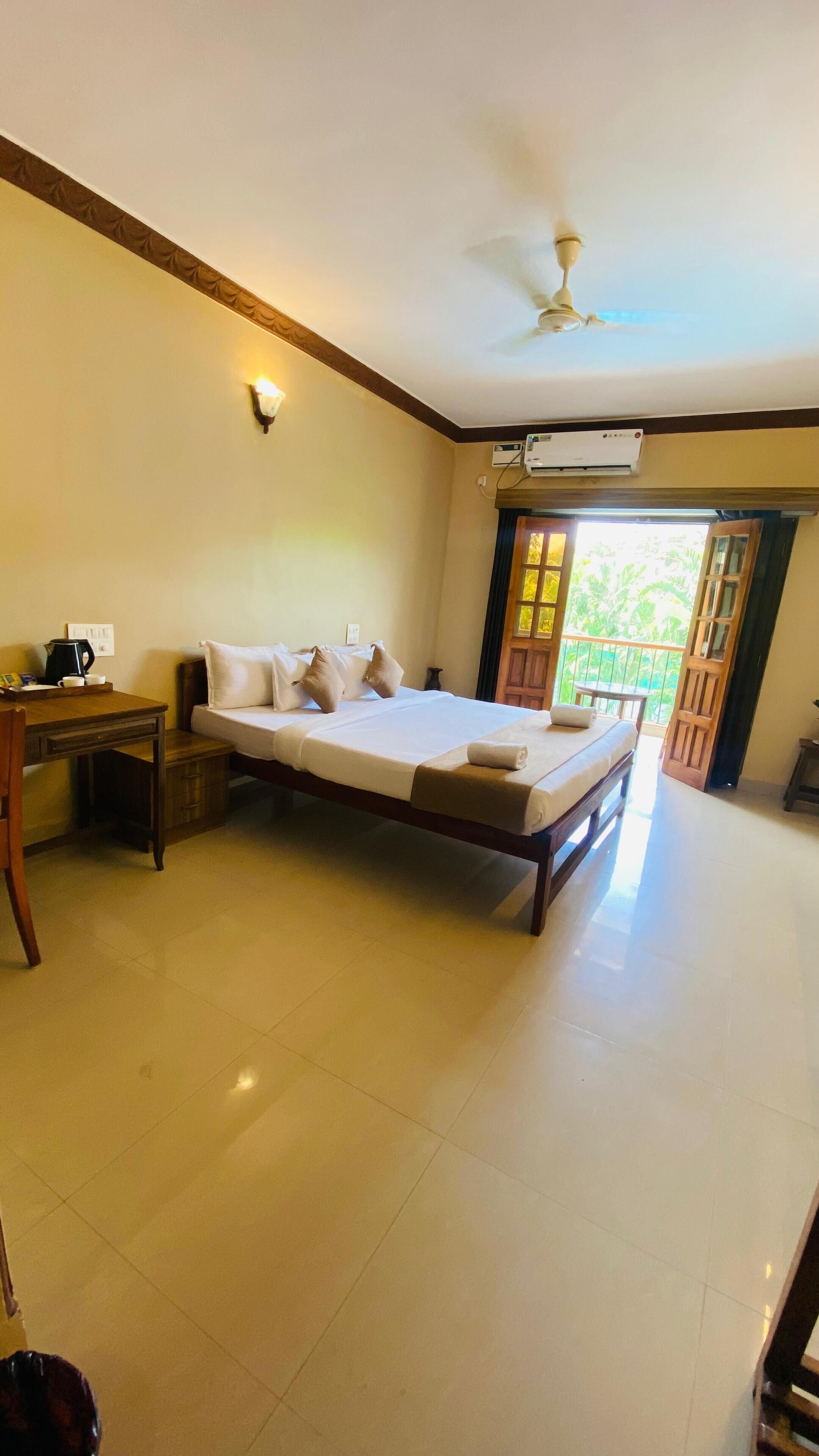 A hotel room with a bed, a desk, a chair, a coffee maker, a ceiling fan, and an air conditioning unit.