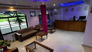 Een hotellobby met een receptiebalie, een zithoek en grote ramen.