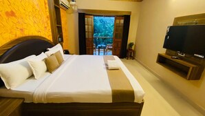 Een hotelkamer met een groot bed, een televisie en een balkon met uitzicht op groen.
