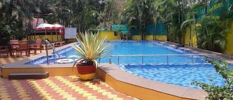 Una piscina con solárium empedrado, rodeada de palmeras y una valla.