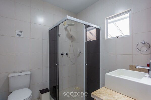 Un baño moderno con ducha de vidrio, inodoro blanco y lavamanos sobre encimera color beige.